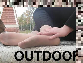 A bad girl plays with her pretty feet while outdoors