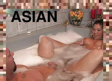 Pierced Asian masseuse giving a handjob to a client in a soapy bath