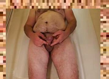 Obese hairy man plays with his dick while standing in bathtub before taking shower