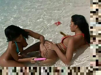 Two hot brunettes fuck each other's assholes with a toy on a beach