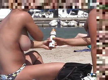 Topless girls lotion each other up on the beach